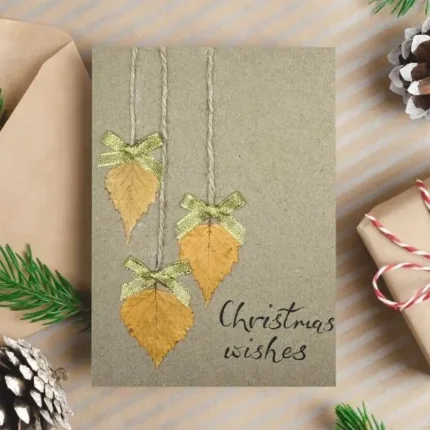 Handmade-Christmas-card-features-dried-leaves-gold-bows-and-Christmas-wishes-text