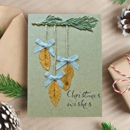 Handmade-Christmas-card-with-three-dried-leaves-and-blue-bows-and-Christmas-wishes